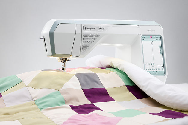 Embroidery machine stitching a colorful quilt on a white background