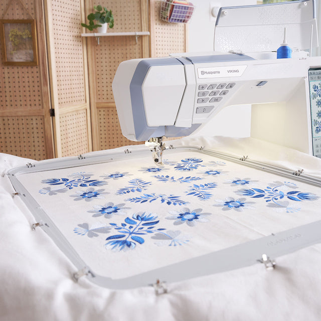 Máquina de bordar con diseños florales azules sobre tela blanca.