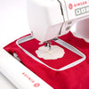 A white Singer hd9120 embroidery machine with a white hoop holding red fabric, stitching a cream-colored flower motif onto the fabric.